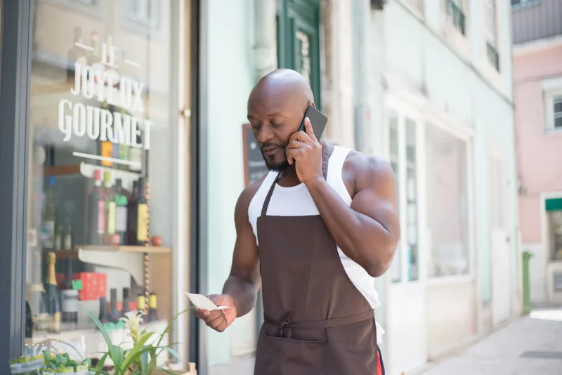Small business owner checking notes on a phone call outside their shop
