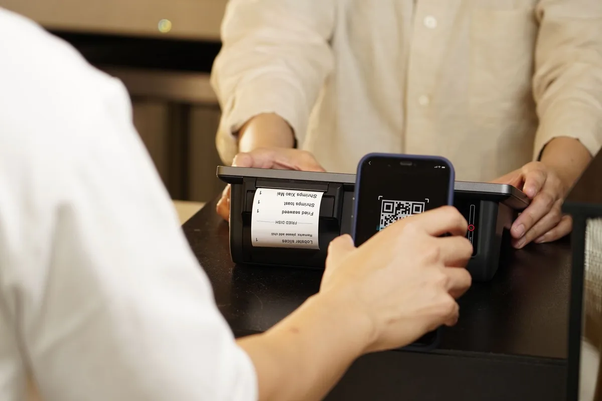 Two people completing a contactless QR code payment at a retail counter in Indonesia