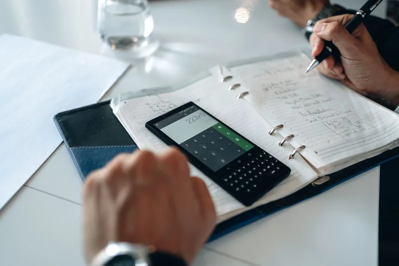 Phone calculator on an open notebook while someone writes out costs