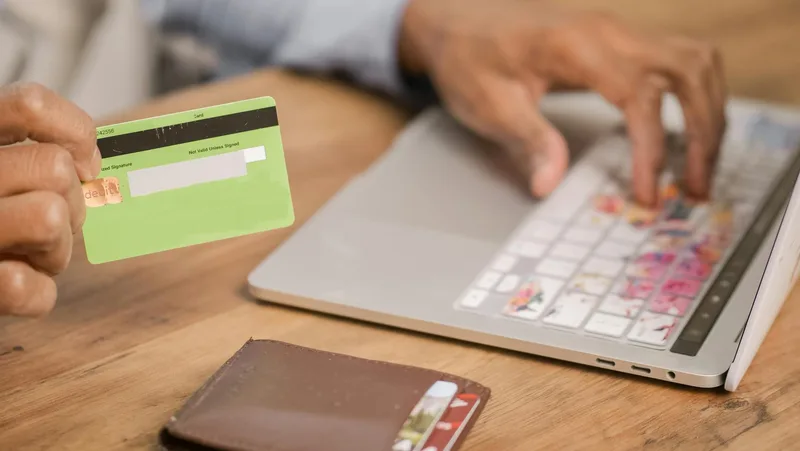 Person using a credit card and laptop to process an online purchase at checkout