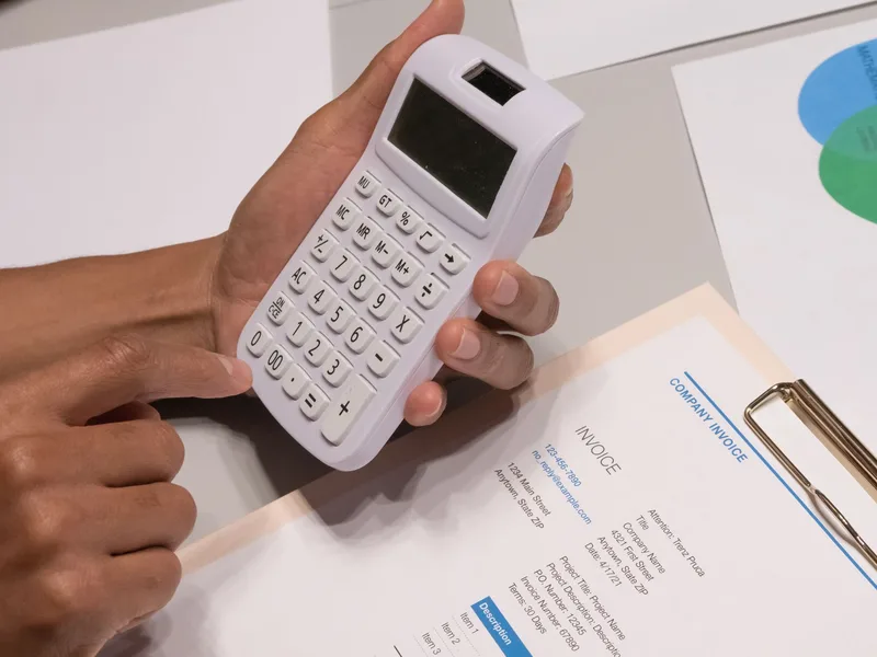 Close-up of hands calculating figures on a business invoice — UAE VAT and AED currency calculations